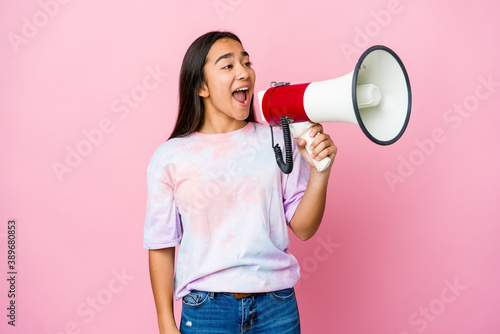 Young asian woman holding a megaphone isolated on pink background shouting and holding palm near opened mouth.