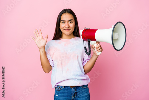 Young asian woman holding a megaphone isolated on pink background smiling cheerful showing number five with fingers.