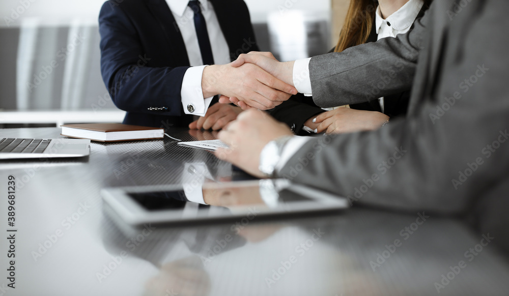 Unknown businessman shaking hands with his colleague or partner above the glass desk in modern office, close-up. Business people group at meeting Unknown businessman shaking hands with his colleague or partner above the glass desk in modern office, close-up. Business people group at meeting