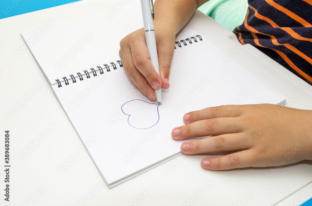 child's hand draws a heart on a white notepad. child's hand draws a heart on a white notepad.