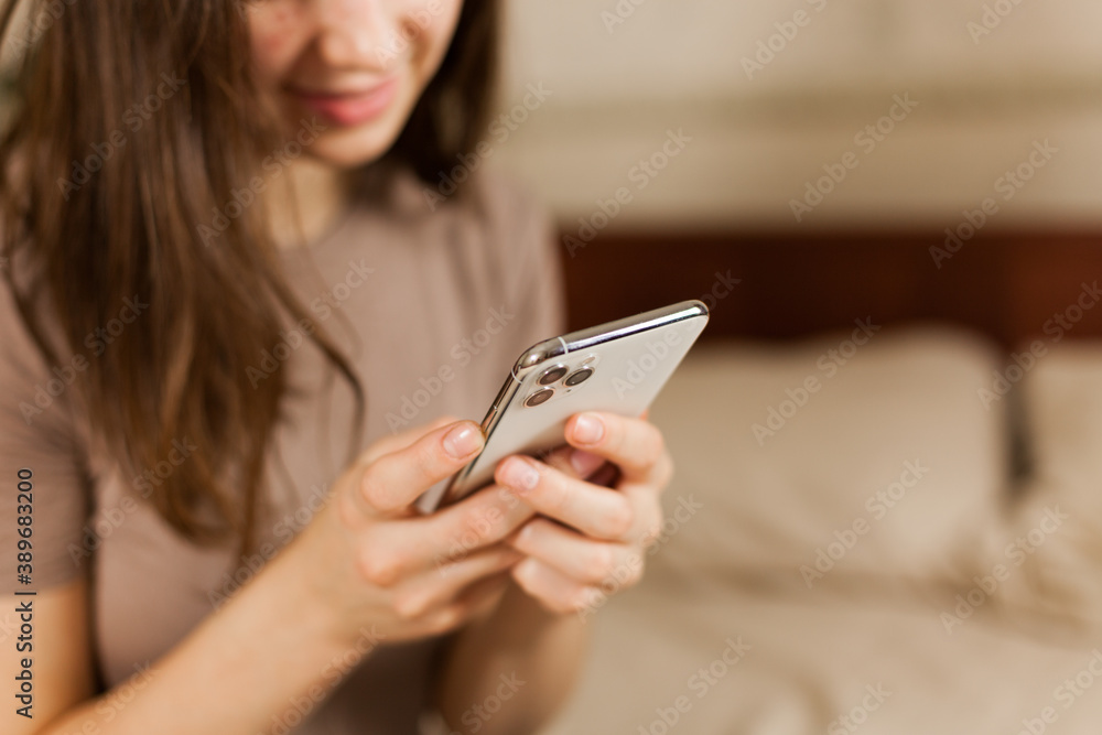 girl smiles and holds in her hand a modern phone with 3 cameras in the bedroom in beige color. communication by phone girl smiles and holds in her hand a modern phone with 3 cameras in the bedroom in beige color. communication by phone