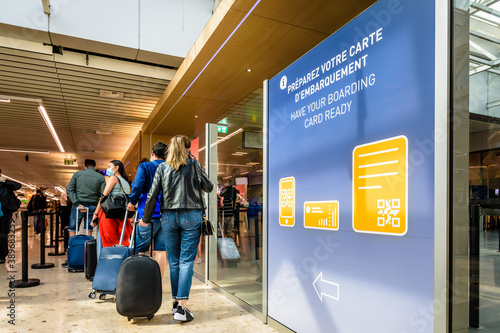 Passengers with cabin luggages stand in line at a checkpoint in the airport concourse next to a sign inviting them to get their boarding pass ready.