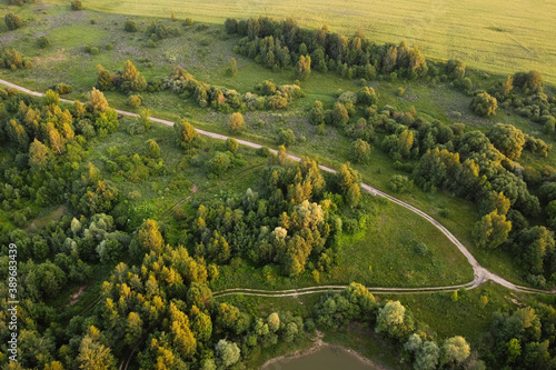 Aerial view of rural road between green field and forest.