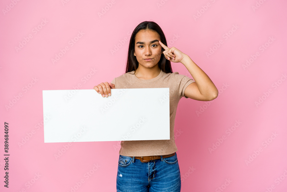 Young asian woman holding a blank paper for white something over isolated background pointing temple with finger, thinking, focused on a task. Young asian woman holding a blank paper for white something over isolated background pointing temple with finger, thinking, focused on a task.