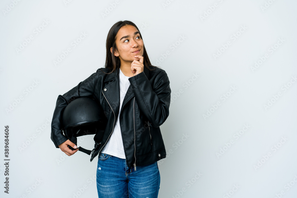 Young asian woman holding a motorbike helmet over isolated background looking sideways with doubtful and skeptical expression. Young asian woman holding a motorbike helmet over isolated background looking sideways with doubtful and skeptical expression.