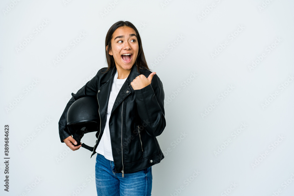 Young asian woman holding a motorbike helmet over isolated background points with thumb finger away, laughing and carefree. Young asian woman holding a motorbike helmet over isolated background points with thumb finger away, laughing and carefree.