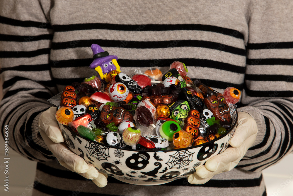 Woman at the front door offering Halloween candies on a nice bowl. Protect for COVID-19. Unrecognizable person
