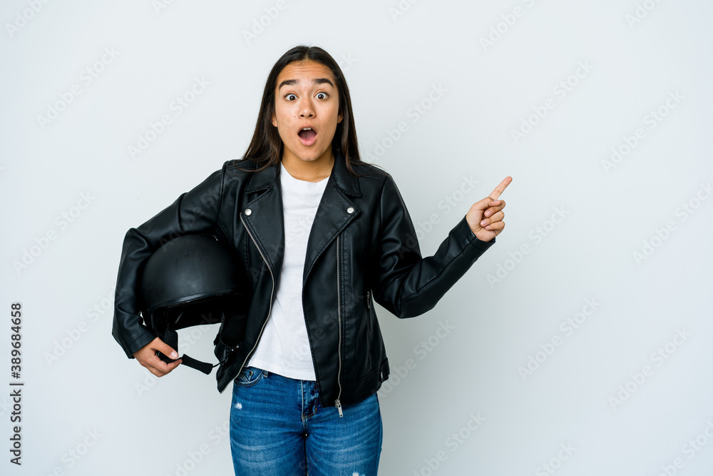 Young asian woman holding a motorbike helmet over isolated background pointing to the side Young asian woman holding a motorbike helmet over isolated background pointing to the side