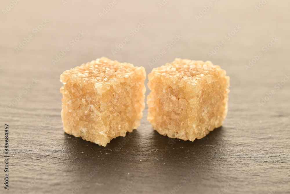 Two cubes of brown sugar, close-up, on a slate board. Two cubes of brown sugar, close-up, on a slate board.