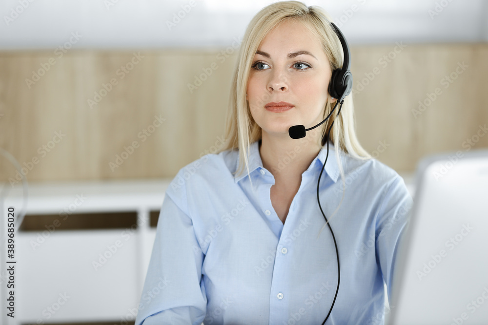 Blonde business woman sitting and communicated by headset in call center office. Concept of telesales business or home office occupation Blonde business woman sitting and communicated by headset in call center office. Concept of telesales business or home office occupation