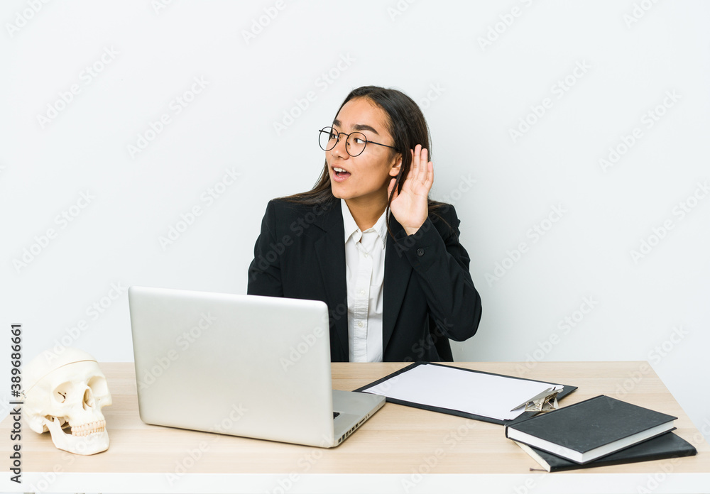 Young traumatologist asian woman isolated on white background trying to listening a gossip. Young traumatologist asian woman isolated on white background trying to listening a gossip.