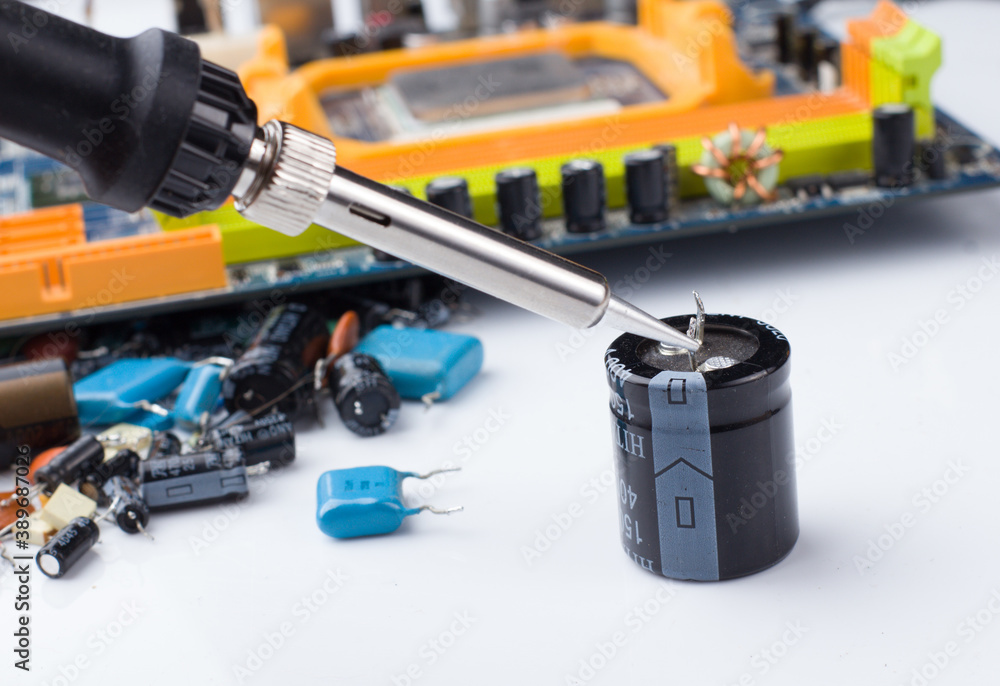 soldering iron on the background of a computer Board and capacitors in soft focus. soldering iron on the background of a computer Board and capacitors in soft focus.