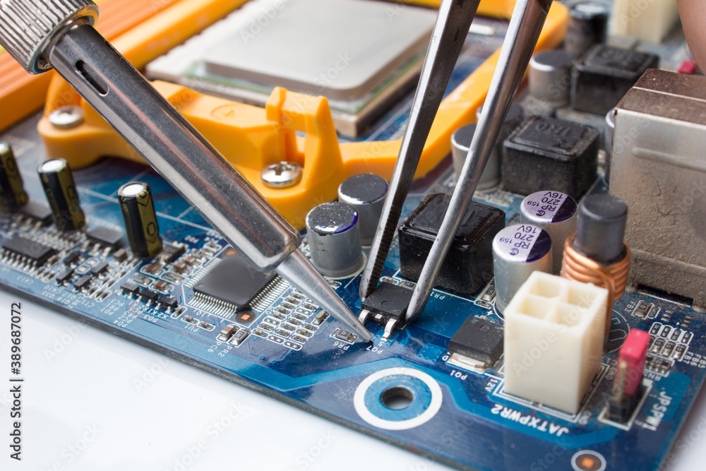 A MOSFET transistor key is soldered out of computer Board using a soldering iron and tweezers