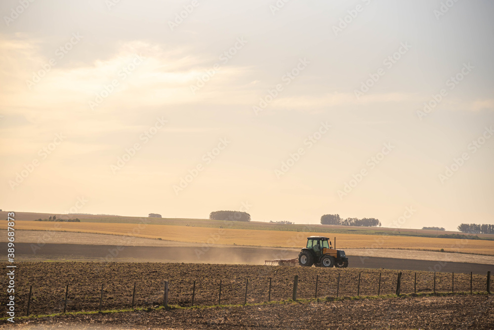 Fototapeta premium Agricultural tractor preparing field for sowing and background landscape of the pampa biome in Brazil