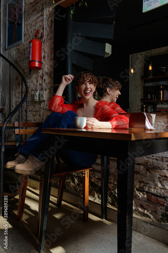 caucasian young woman curly hair  red shirt and jeans with cup cake and cup of coffee