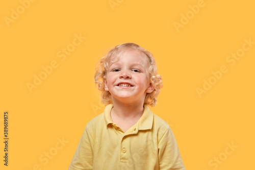 Funny beautiful blond boy on a yellow isolated background looks at the camera. Human emotion.