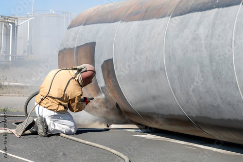 The sandblaster is sanding to steel pipe material. Abrasive blasting, more commonly known as sandblasting, is the operation of forcibly propelling a stream of abrasive material against a surface . photo