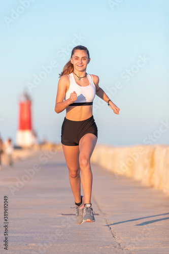 City running - Young teenager girl runner runs along the boardwalk during sunset