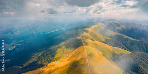Flying under the clouds. Panoramic summer view from flying drone of Krasna range with old country road. Misty morning view of Carpathian mountains, Ukraine, Europe. Traveling concept background.