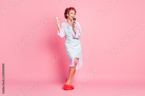 Full size photo of happy beautiful young woman hold salt pepper wear bathrobe hair curlers isolated on pastel pink color background