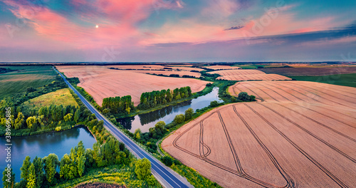 Fantastic summer sunset on the Ternopil outskirts with two lakes and asphalt road. Breathtaking morning view of the Ukrainian countryside. Amazing landscape of field of wheat.
