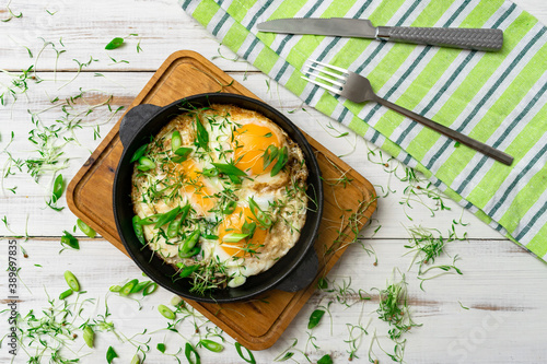 scrambled eggs with greens sprouts and green onions in a pan on a wooden background.