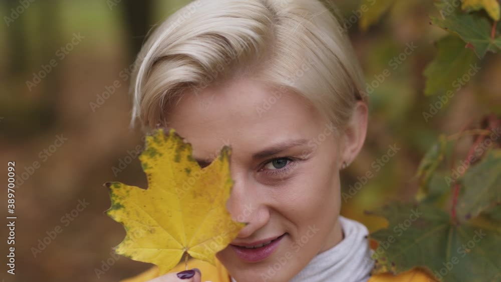 Portrait shot of young caucasian blonde woman with blue eyes hiding face with yellow autumn leaf Portrait shot of young caucasian blonde woman with blue eyes hiding face with yellow autumn leaf