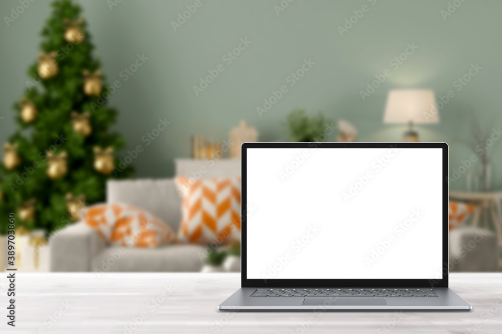 Fototapeta premium Blank display screen laptop computer on white wood table. Modern cozy comfortable home living room with Christmas decor. Home office desk workspace. Mock up copy space. Winter sales, online shopping