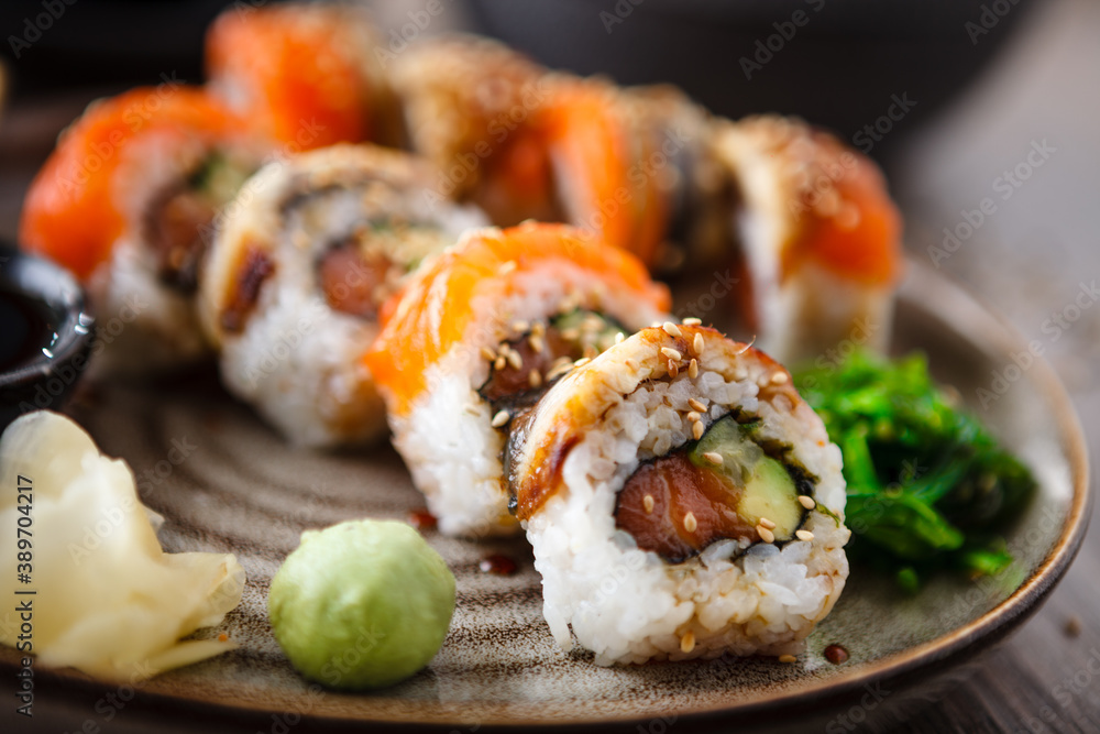 Sushi maki rolls with salmon, eel, avocado, cucumber on a plate with chopsticks, soy sauce, wasabi and ginger. Japanese traditional fish food closeup served for lunch in modern gourmet restaurant Sushi maki rolls with salmon, eel, avocado, cucumber on a plate with chopsticks, soy sauce, wasabi and ginger. Japanese traditional fish food closeup served for lunch in modern gourmet restaurant