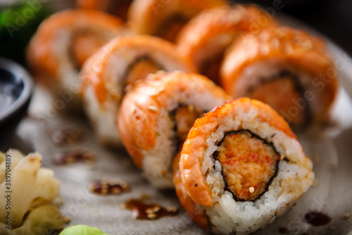 Baked sushi maki rolls with salmon, crab and spicy sauce on a plate with chopsticks, soy sauce, wasabi and ginger. Japanese traditional fish food closeup served for lunch in modern gourmet restaurant