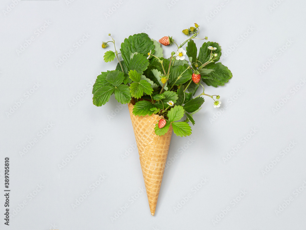 Waffle cone with leaves, flowers and strawberries on a grey background. Flat lay. A concept photo is an original gift. Healthy, right food.