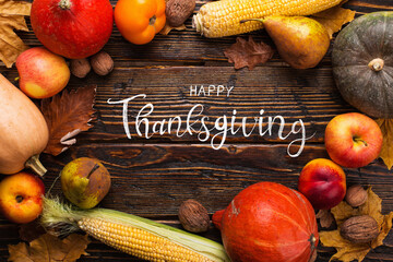 Thanksgiving greetings. Pumpkins, vegetables, nuts, dry leaves on a wooden background, top view. Kaligraphic capital inscription.