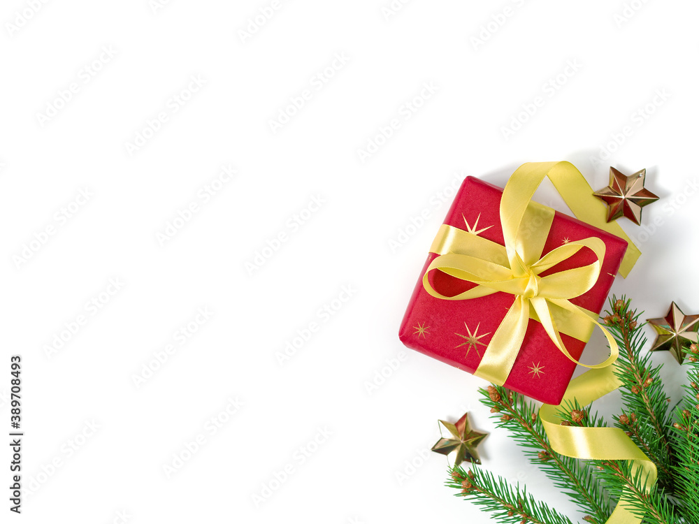 The gift wrapped in red wrapping paper is tied with a yellow ribbon with a bow. A natural spruce branch and golden stars are nearby. Christmas composition. Flat lay. Top view. Copy space.