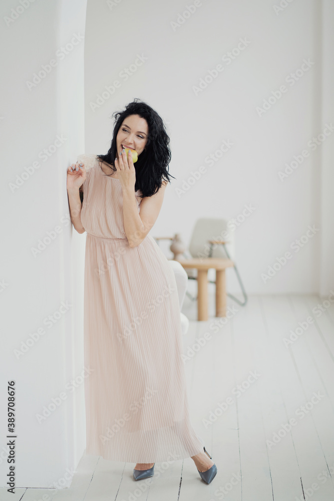 a young brunette woman poses for the camera eating an Apple in a new stylish beige dress and stylish shoes with heels. holiday clothing a young brunette woman poses for the camera eating an Apple in a new stylish beige dress and stylish shoes with heels. holiday clothing
