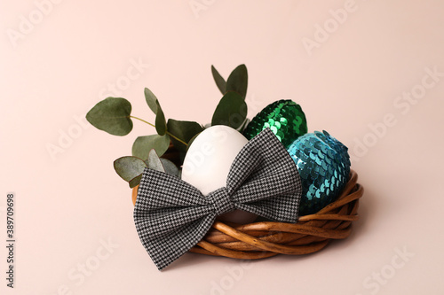 Natural egg in the bow tie in the rattan nest.Fresh eucalyptus branch on the background.Pastel color,copy space for text.Easter concept.