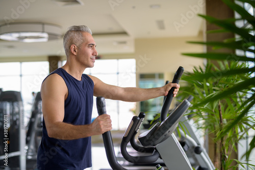 Mature Persian man exercising with elliptical trainer machine at the gym