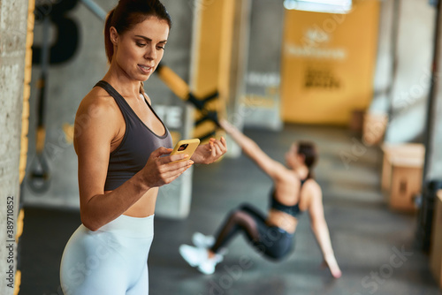 Young focused sportive woman using smartphone while exercising at gym