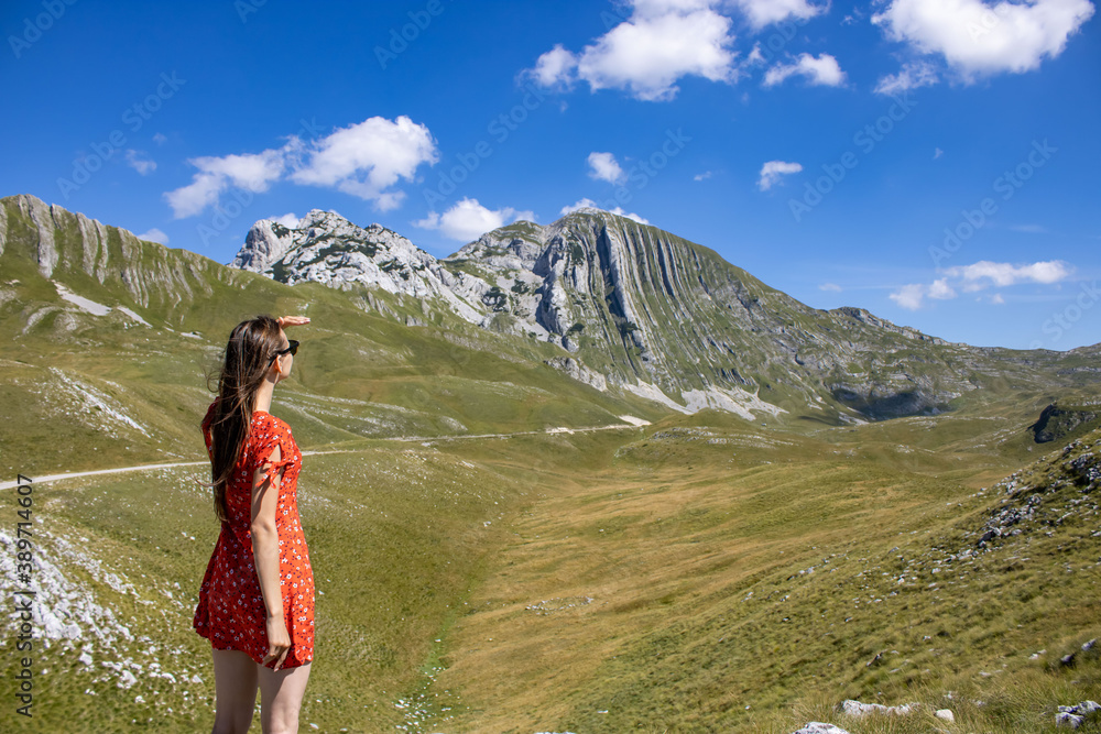 The girl in a red dress against the background of the mountains of Montenegro. Picturesque mountain landscape of Durmitor National Park, Montenegro, Balkans, Dinaric Alps, UNESCO World Heritage Site.
