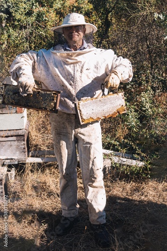Beekeeper in a protective bee suit showing two beautiful honeycombs