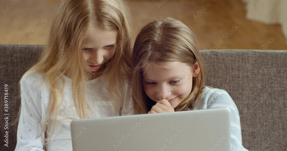 Smiling young two small kids enjoying using laptop together watching funny cartoons videos laughing playing online surfing web on modern computer device relaxing sitting on sofa at home in living room Smiling young two small kids enjoying using laptop together watching funny cartoons videos laughing playing online surfing web on modern computer device relaxing sitting on sofa at home in living room