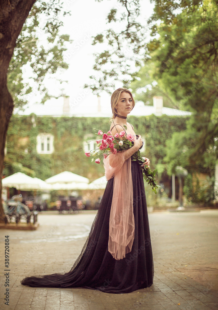 
girl in a black dress and a bouquet of flowers on the street of the old city