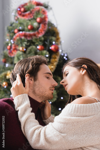 side view of passionate couple embracing near decorated christmas tree on blurred background