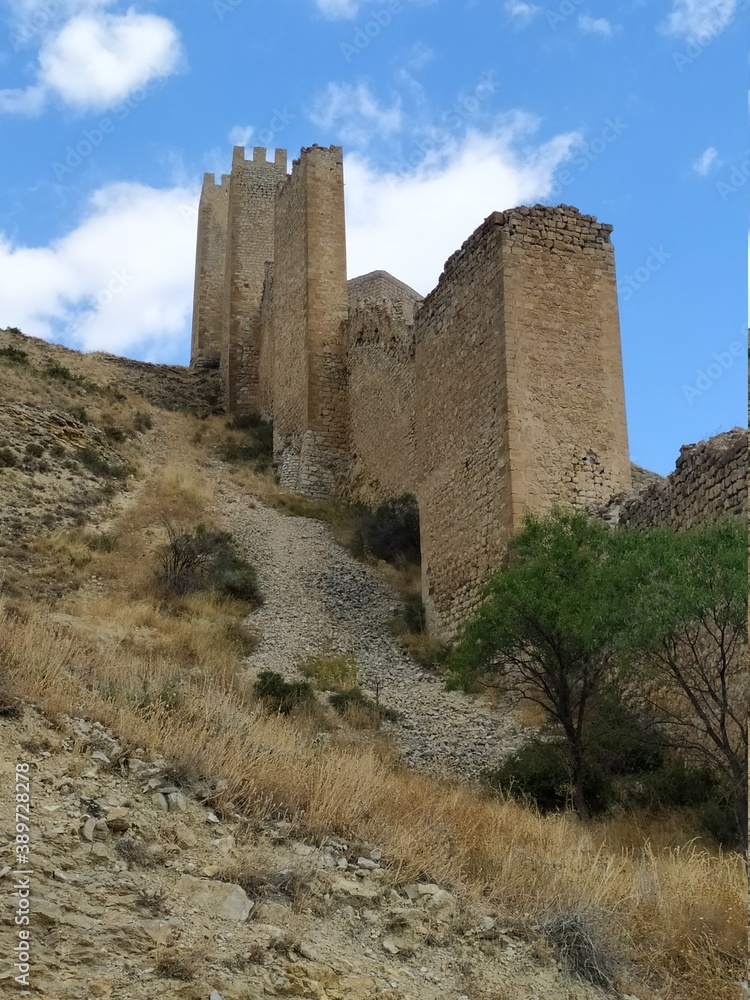 Muralla de castillo en ruinas en ladera de montaña con cielo azul