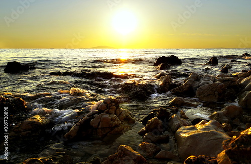 Beautiful shiny and sparkling sea sunset above stony beach and shallow water rippled between rocks