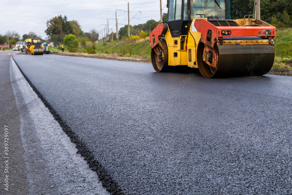 Asphalt road roller with heavy vibration roller compactor press new hot asphalt on the roadway on a road construction site. Heavy Vibration roller at asphalt pavement working. Repairing. Asphalt road roller with heavy vibration roller compactor press new hot asphalt on the roadway on a road construction site. Heavy Vibration roller at asphalt pavement working. Repairing.