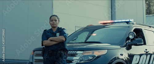 Mixed race female police officer posing against police car with flashing lights