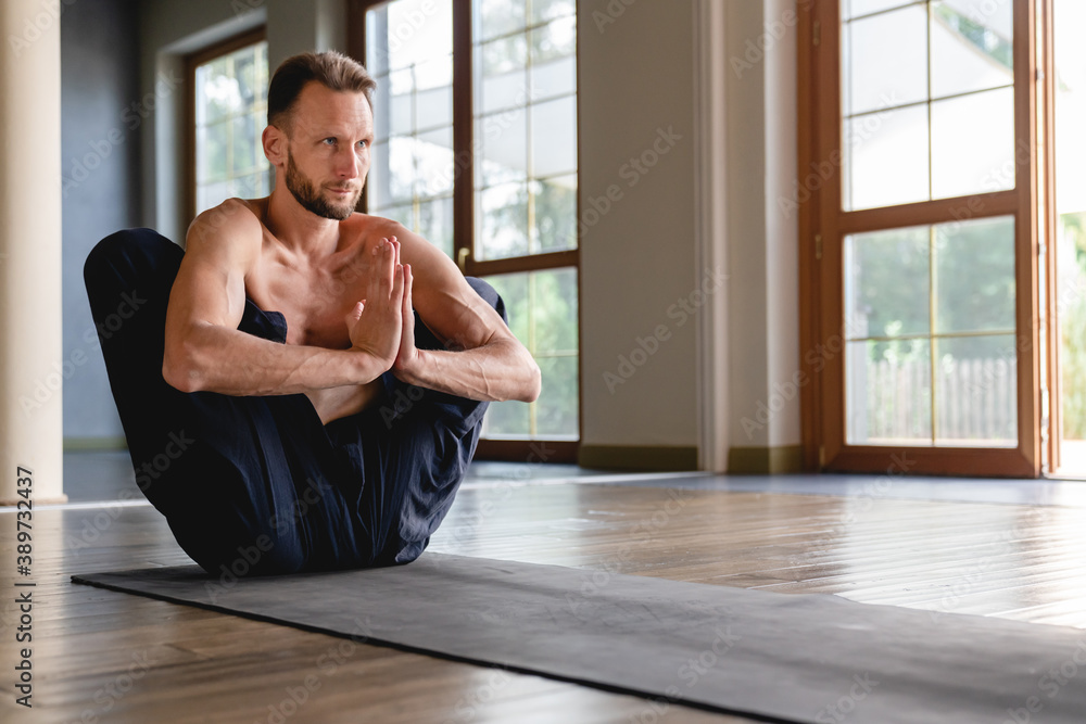 Attractive caucasian flexible yogi man concentrating in lotus position in light roomy studio Attractive caucasian flexible yogi man concentrating in lotus position in light roomy studio