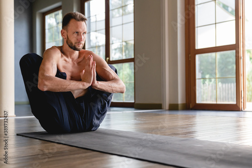Attractive caucasian flexible yogi man concentrating in lotus position in light roomy studio