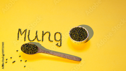 Mung beans in a ceramic sauce pan, in a wooden spoon and scattered on the surface. The inscription. Copy space, healthy food, design.