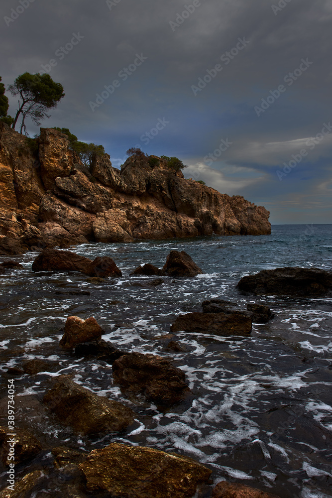 Seascape of a rocky coast that juts out into the Mediterranean Sea, at sunset, with a cloudy sky